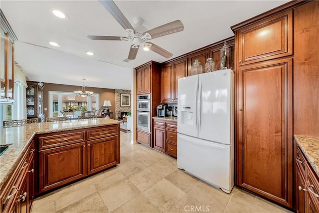 kitchen featuring hanging light fixtures, ceiling fan with notable chandelier, white refrigerator with ice dispenser, and light stone countertops