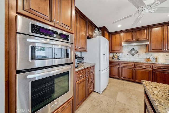 kitchen featuring ceiling fan, double oven, backsplash, light stone countertops, and white fridge with ice dispenser