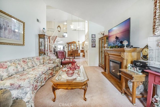 1308 Pleasant Valley Ave, Banning, CA 92220 - living room with light carpet, a high ceiling, visible vents, stairs, and a glass covered fireplace