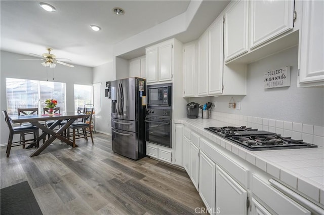 kitchen featuring white cabinetry, tile countertops, dark hardwood / wood-style flooring, and black appliances