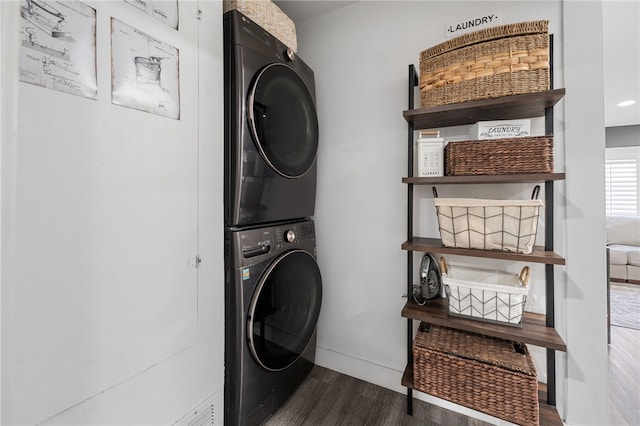 clothes washing area featuring laundry area, stacked washer and dryer, baseboards, and wood finished floors