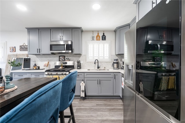 kitchen featuring gray cabinets, decorative backsplash, appliances with stainless steel finishes, a sink, and light wood-style floors