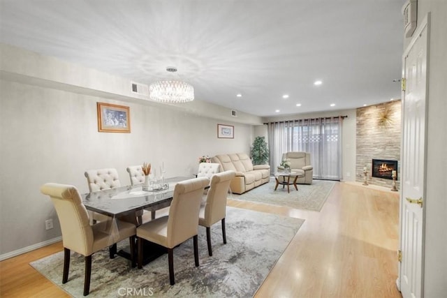 dining room featuring a tiled fireplace, hardwood / wood-style floors, and an inviting chandelier