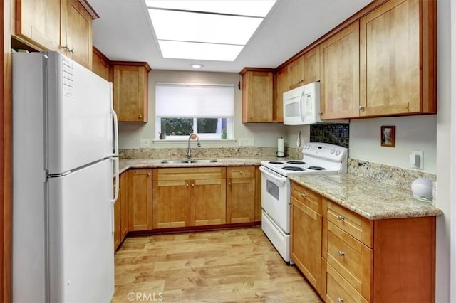 kitchen featuring sink, white appliances, light hardwood / wood-style flooring, a skylight, and light stone counters