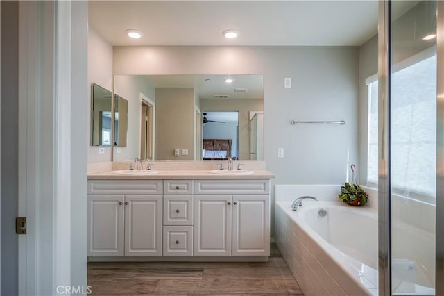 bathroom with a garden tub, double vanity, wood finished floors, and a sink