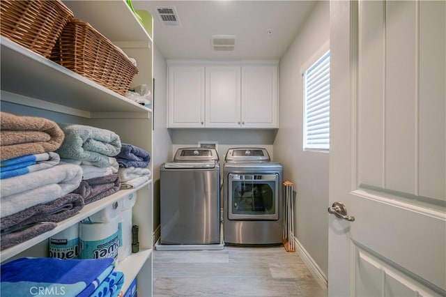 clothes washing area featuring separate washer and dryer, visible vents, baseboards, light wood-type flooring, and cabinet space