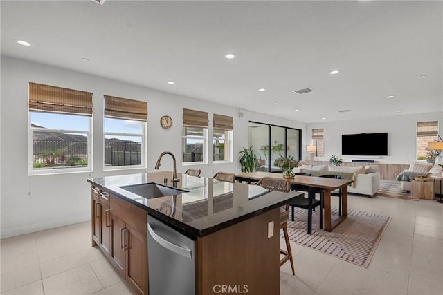 kitchen featuring light tile patterned flooring, an island with sink, sink, dark stone counters, and stainless steel dishwasher