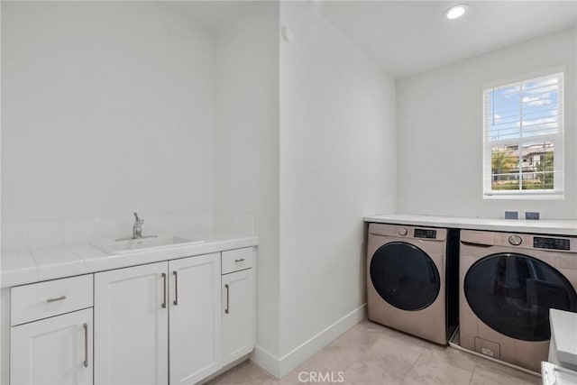 clothes washing area with cabinets, washing machine and clothes dryer, and sink