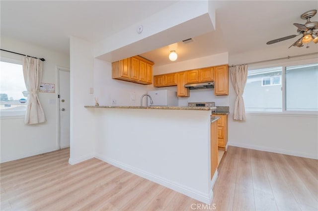 kitchen with white refrigerator, kitchen peninsula, ceiling fan, light stone countertops, and light hardwood / wood-style floors