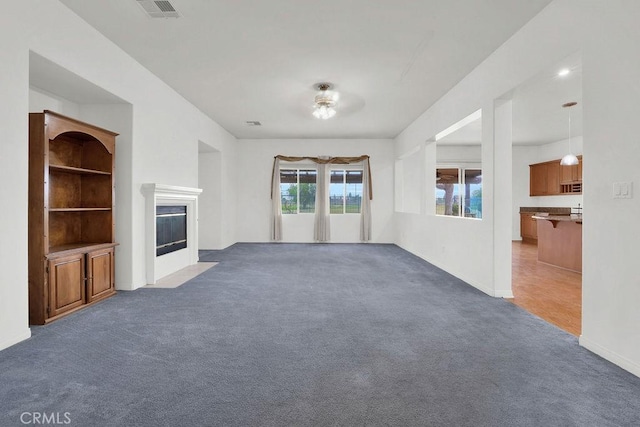 unfurnished living room with baseboards, visible vents, a fireplace with flush hearth, and carpet