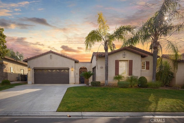 mediterranean / spanish house with a lawn, a garage, driveway, and stucco siding