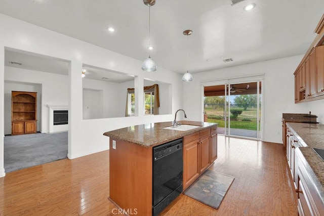 kitchen with a sink, light wood-style floors, dishwasher, dark stone counters, and visible vents