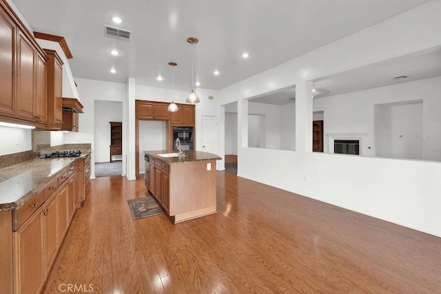 kitchen featuring a kitchen island with sink, visible vents, open floor plan, stainless steel gas stovetop, and light wood-style flooring