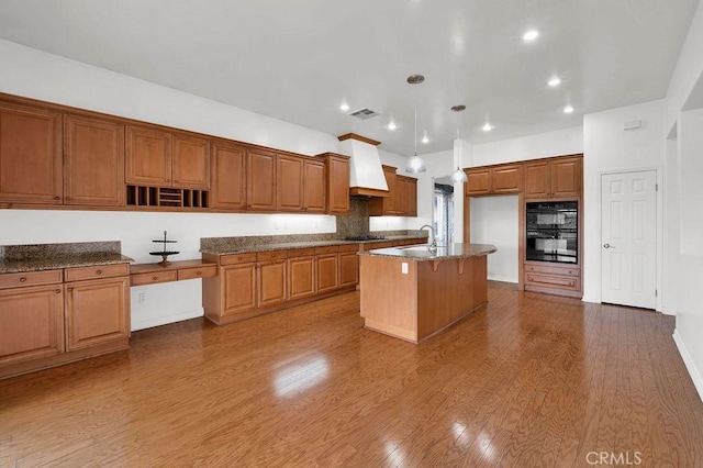 kitchen with dobule oven black, visible vents, wood finished floors, brown cabinets, and a sink