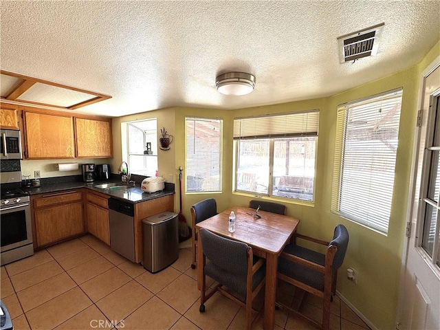 kitchen featuring brown cabinetry, dark countertops, stainless steel appliances, and visible vents