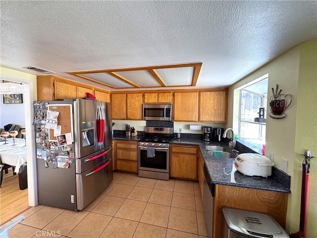 kitchen with brown cabinetry, a textured ceiling, stainless steel appliances, and a sink