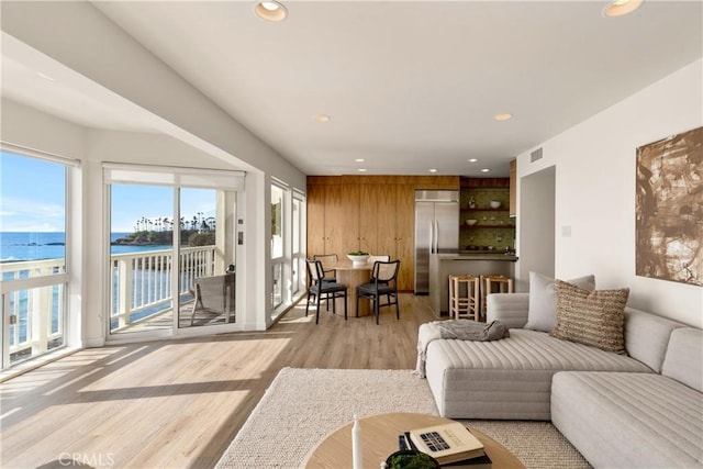 living room with a water view, wooden walls, and light hardwood / wood-style floors