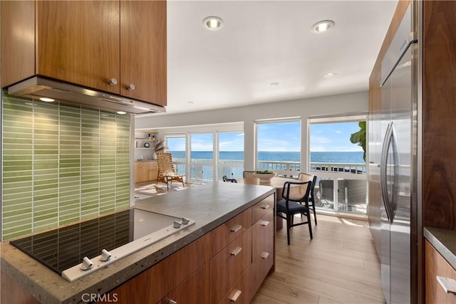 kitchen featuring stainless steel refrigerator, a water view, tasteful backsplash, light hardwood / wood-style floors, and black electric cooktop