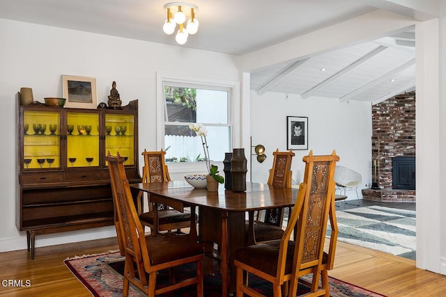 dining space with wood-type flooring, lofted ceiling with beams, and a brick fireplace