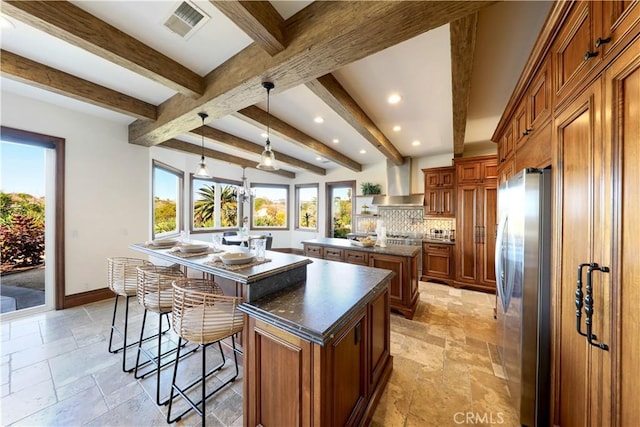 kitchen featuring a kitchen bar, decorative light fixtures, a center island, stainless steel refrigerator, and wall chimney range hood