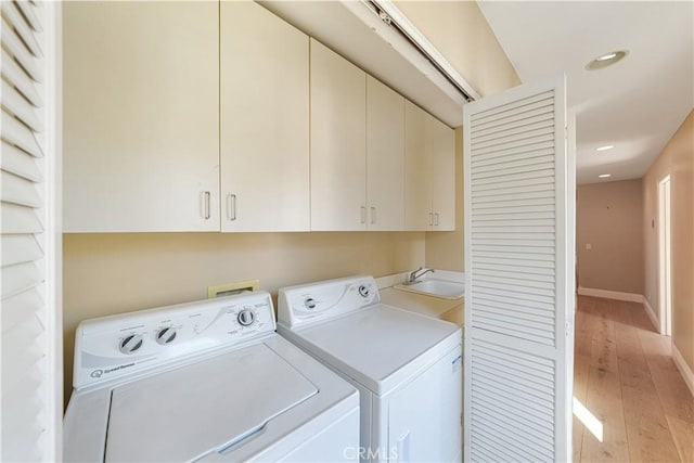 laundry room featuring independent washer and dryer, sink, light hardwood / wood-style floors, and cabinets