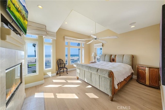 bedroom with a tile fireplace, a water view, ceiling fan, and light wood-type flooring