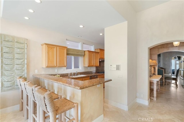 kitchen featuring sink, a kitchen bar, stainless steel dishwasher, light stone counters, and kitchen peninsula