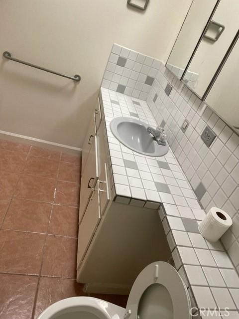 half bath with tile patterned floors, vanity, baseboards, and toilet