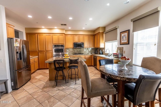 kitchen with a center island, visible vents, backsplash, light stone countertops, and black appliances