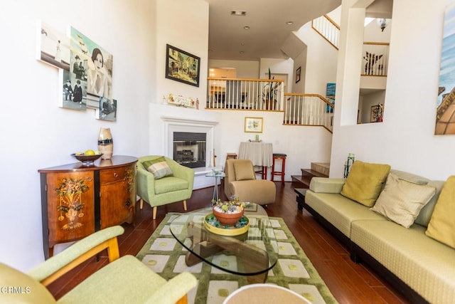 living room with stairs, dark wood-style flooring, a glass covered fireplace, and visible vents