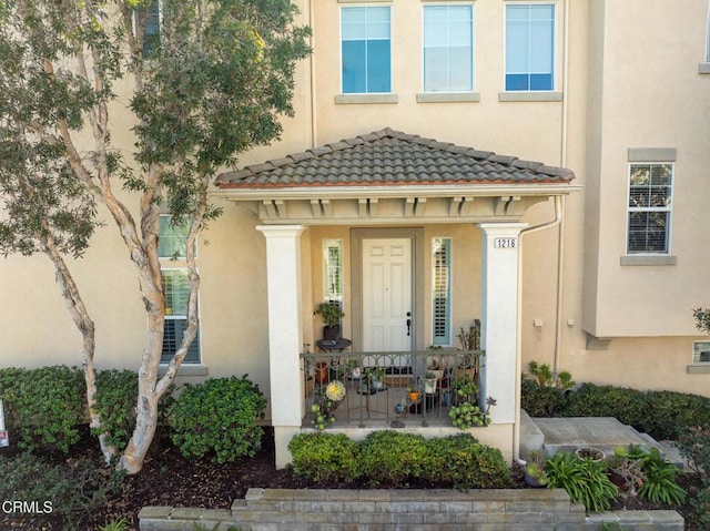 entrance to property featuring a porch, a tile roof, and stucco siding