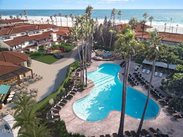 view of swimming pool with a water view, a beach view, and a patio area