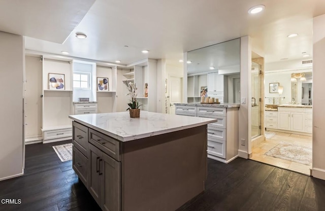 kitchen with dark wood-type flooring, a center island, light stone countertops, and white cabinets