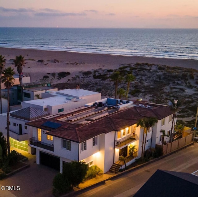 aerial view at dusk featuring a view of the beach and a water view