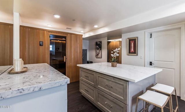 kitchen with light stone countertops, a kitchen island, dark hardwood / wood-style floors, and a kitchen bar