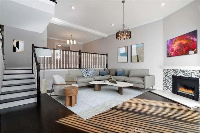 living room with a tile fireplace, wood-type flooring, crown molding, and an inviting chandelier