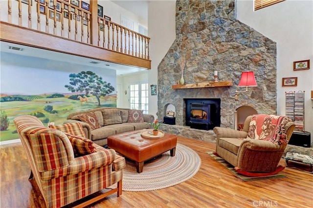 living room featuring a stone fireplace, visible vents, a towering ceiling, and wood finished floors