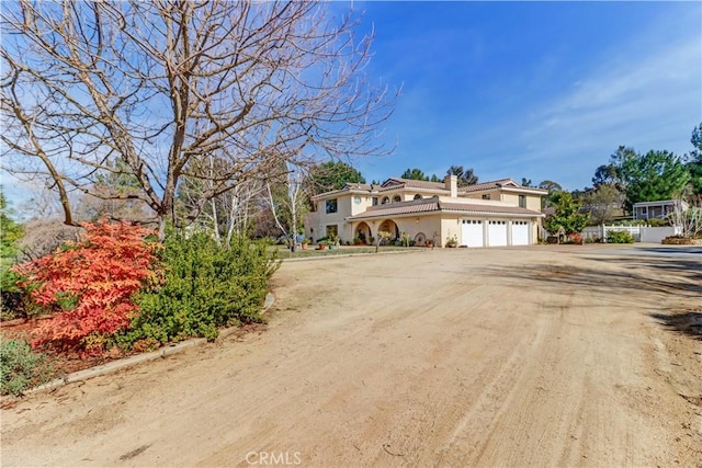 view of front of house featuring dirt driveway, a chimney, an attached garage, and stucco siding