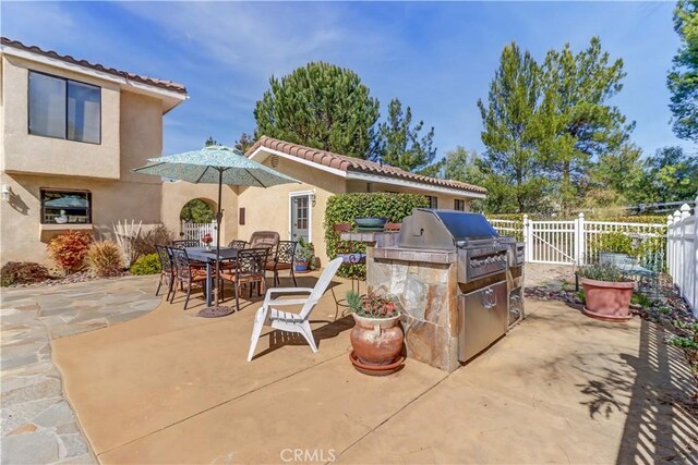 view of patio / terrace with exterior kitchen, outdoor dining space, a grill, and fence