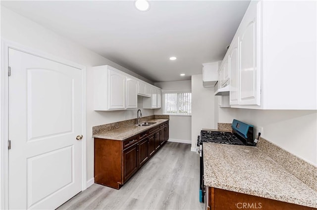 kitchen with sink, light hardwood / wood-style floors, gas range oven, and white cabinets