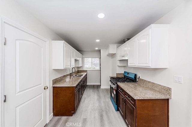 kitchen featuring sink, stainless steel gas stove, white cabinetry, dark brown cabinetry, and light wood-type flooring