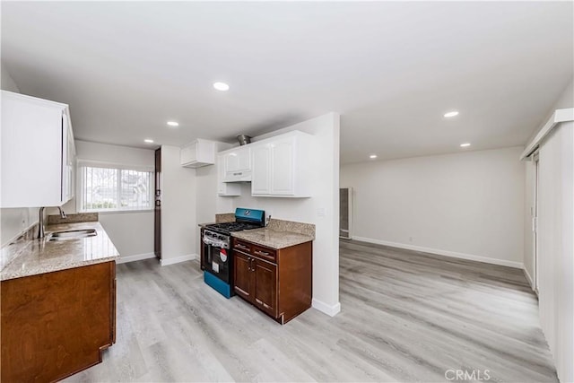 kitchen featuring sink, light hardwood / wood-style floors, light stone countertops, white cabinets, and gas range