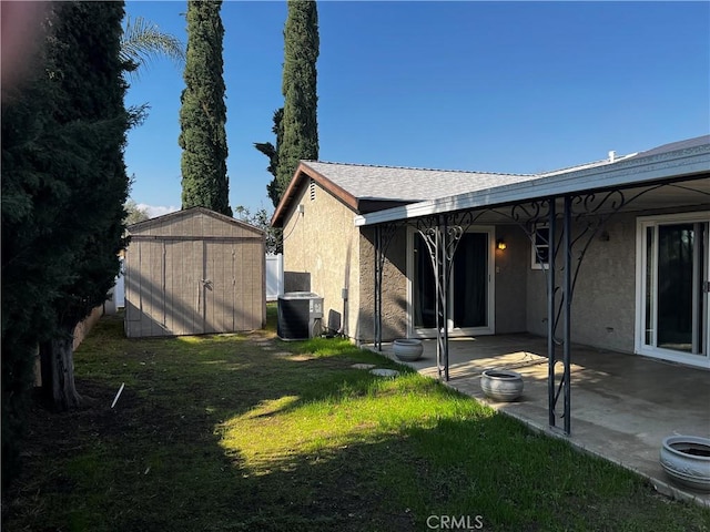 back of house with central AC, a patio, a lawn, and a storage unit