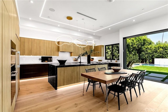 kitchen featuring pendant lighting, sink, a kitchen island with sink, tasteful backsplash, and light hardwood / wood-style floors