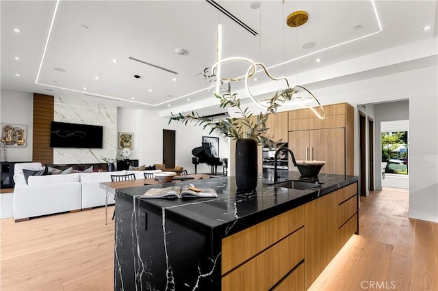 kitchen featuring sink, a tray ceiling, dark stone counters, a large island, and light hardwood / wood-style floors