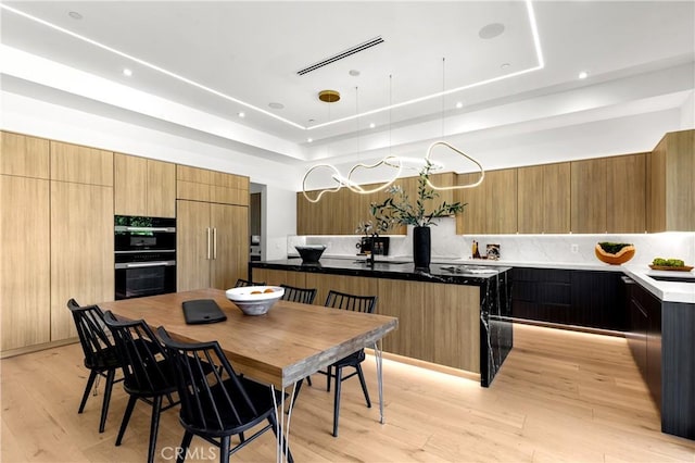 kitchen featuring a center island, paneled built in refrigerator, a tray ceiling, double oven, and light hardwood / wood-style floors