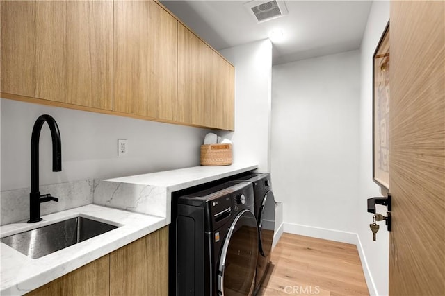 laundry room featuring independent washer and dryer, sink, cabinets, and light wood-type flooring