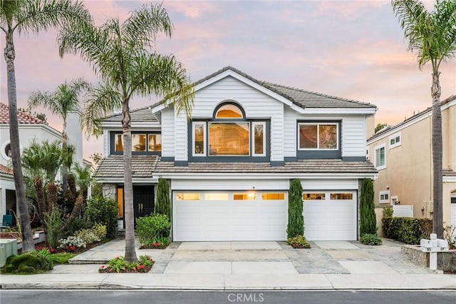 traditional home with a tiled roof, an attached garage, and driveway