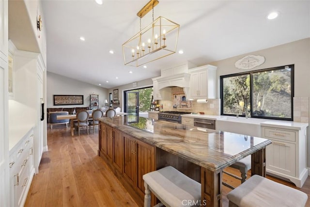 kitchen featuring light stone counters, white cabinetry, vaulted ceiling, tasteful backsplash, and decorative light fixtures