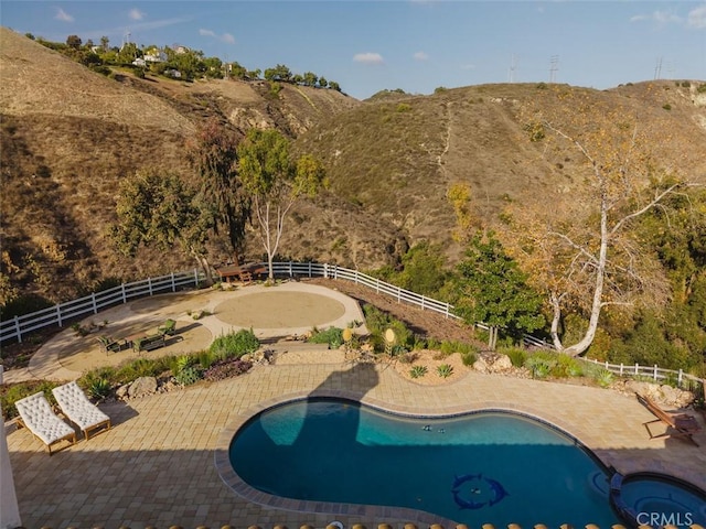 view of swimming pool featuring a pool with connected hot tub, fence, a patio, and a mountain view